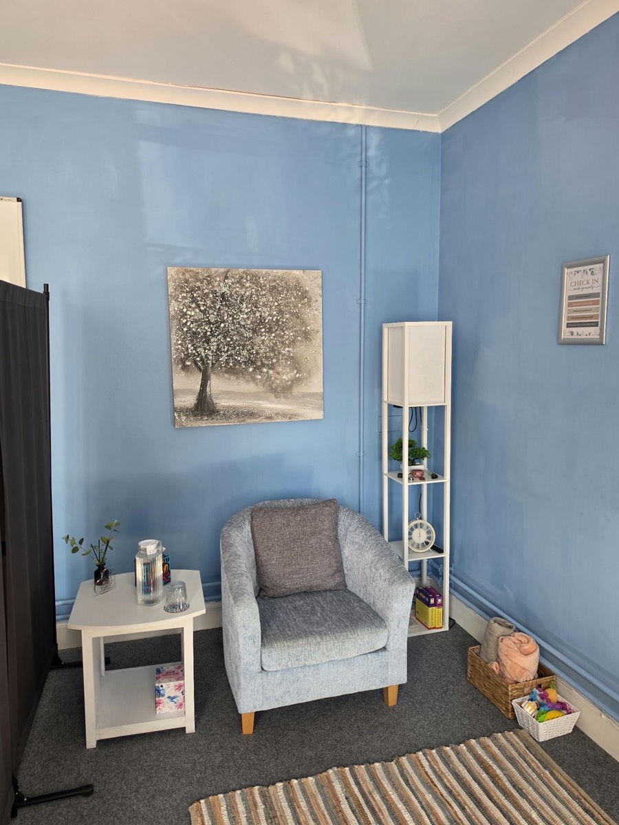 A soft armchair beside a small table, with a tree painting on the wall